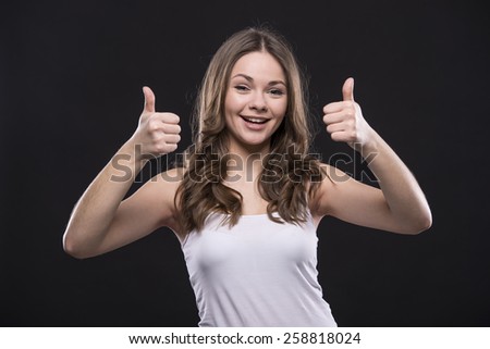 Young woman is showing thumbs up standing on dark background.