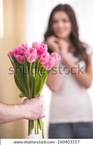 Man is giving a bunch of flowers and happy woman at home. Focus on flowers.