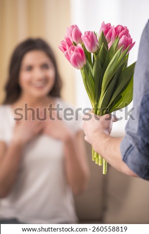 Man is giving a bunch of flowers and happy woman at home. Blurred background.