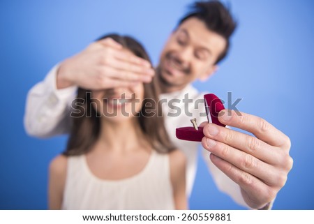 Man is making woman offer get engaged on blue background. Blurred background.