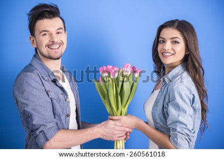 Boyfriend is giving flowers to his beautiful girlfriend isolated on blue background.