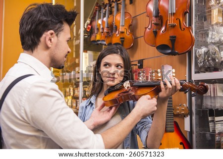 Young man is teaching girl to play the violin at the music store.