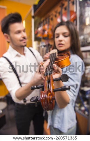 Young man is teaching girl to play the violin at the music store. Blurred background.