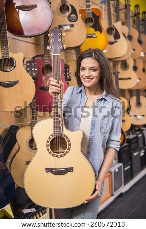 Beautiful young girl is holding a guitar in music store.