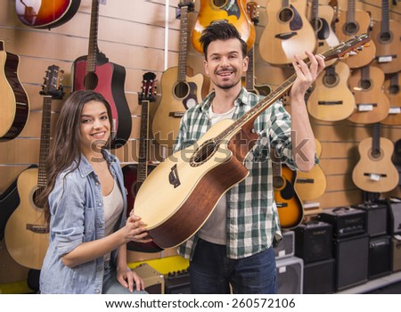 Attractive men and women are choosing a guitar in a music store.