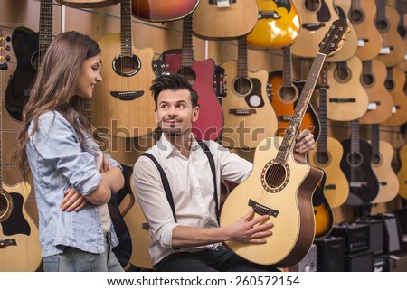 Man is showing to girl guitar background of guitars in a music store.