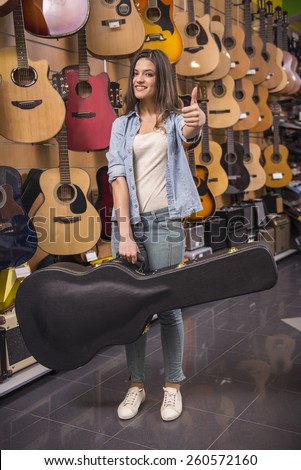 Young girl is holding a guitar in a case and is showing thumb up in a musical instrument.