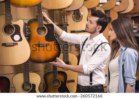 Man and woman are considering a guitars in a music store.