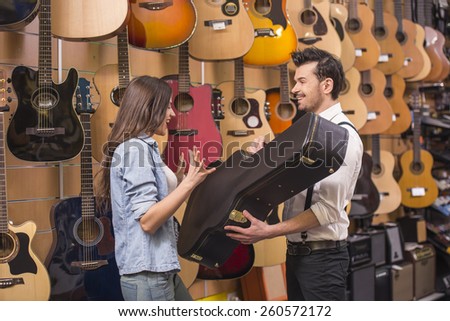 Young girl is buying a guitar in a case in the music store.
