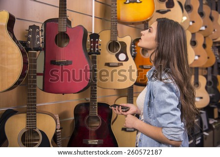 Beautiful young girl is chooses a guitar in music store.