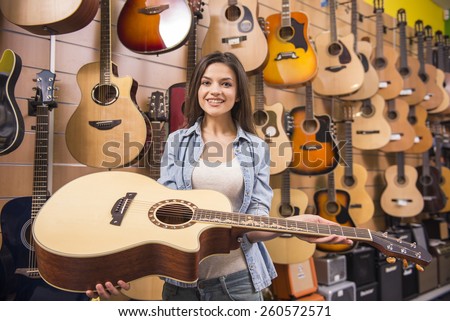 Beautiful young girl is holding a guitar in a music store. Blurred background.