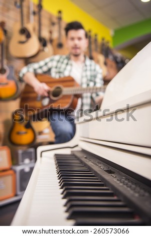 White piano close-up on a background blurry man is playing guitar.