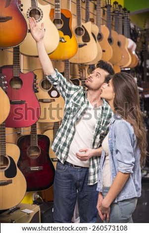 Man is showing to girl guitar in a music store.
