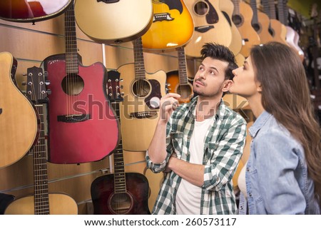 Man and woman are considering a guitars in a music store.