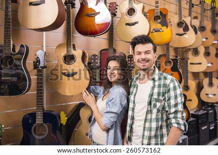 Young man and girl are smiling on the background of guitars in the music store.
