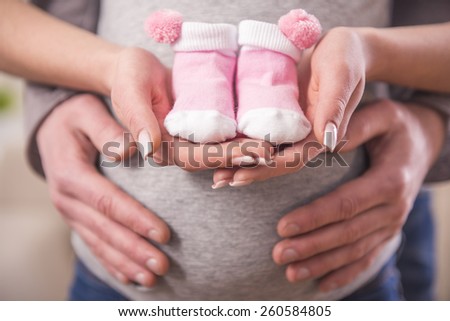 Man and his pregnant wife are trying baby socks on her belly. Close-up.