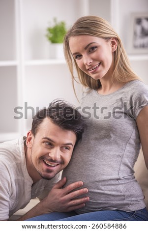 Husband is listening to his pregnant wife\'s belly at home.