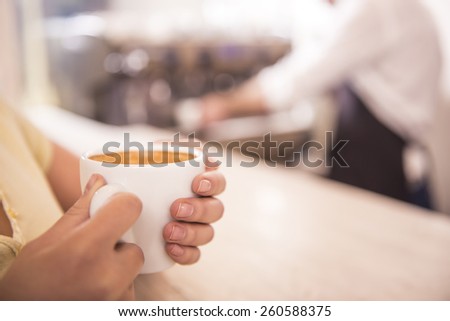 Ã?Â�Ã?Â¡lose-up of a cup of coffee in the hands of women on the background barista. Blurred background.