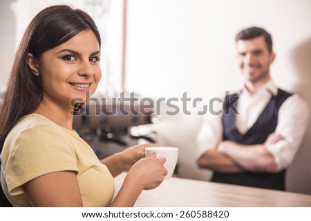 Smiling young woman is holding a coffee at barista. Blurred background.