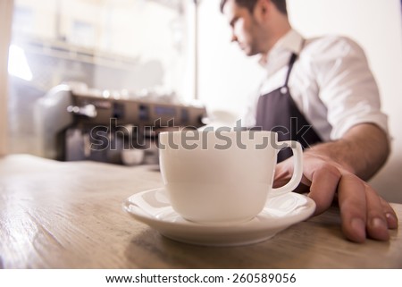 Barista prepares cappuccino in his coffee shop. Close-up cup of coffee.
