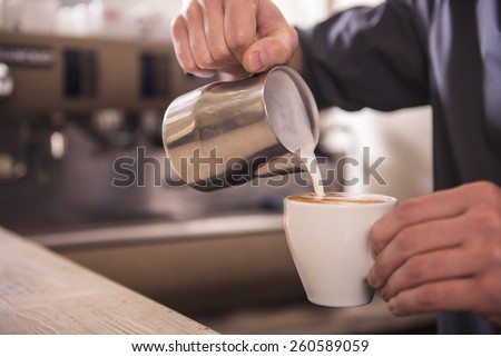Barista hands is pouring milk making cappuccino.