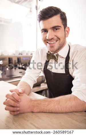 Handsome smiling young barista in his cafe.