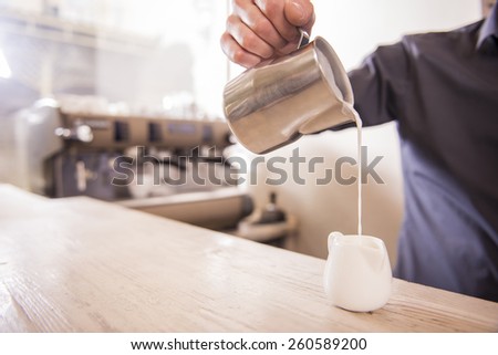 Barista hands is pouring milk making cappuccino.