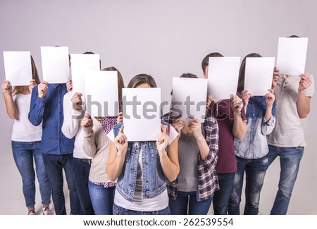 Top view. Portrait of four teenage group holding a white board and cover their faces. isolated on grey background.