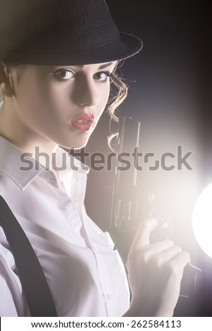 Beautiful and dangerous. Young female gangster holding the gun. isolated on dark background.