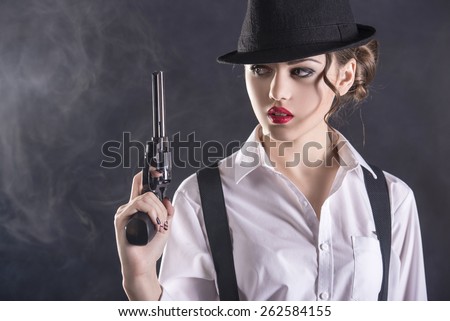 Beautiful and dangerous. Young female gangster holding the gun. isolated on dark background.
