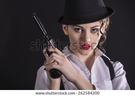 Beautiful and dangerous. Young female gangster holding the gun and looking at camera. isolated on dark background.