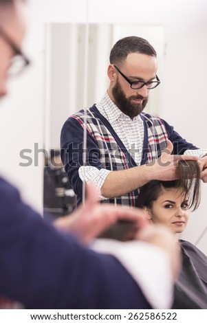 Handsome hairdresser making a haircut for a beautiful brunette girl.