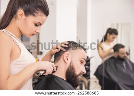 Hairdresser cuts hair with hair clipper on back of the head  in hairdressing salon