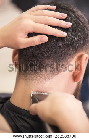 Close-up of hairdresser cutting hair of a male with hair clipper on back of the head  in hairdressing salon.