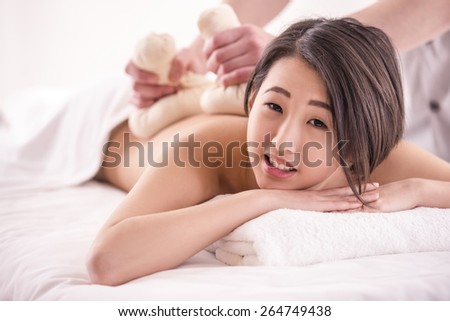 Side view. Beautiful asian woman having massage with spa herbal balls in beauty salon. Looking at camera.