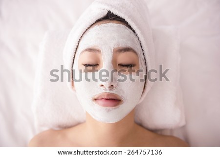 Spa therapy for young asian woman receiving facial mask at beauty salon.