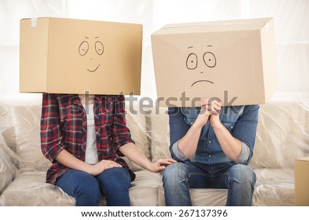 Couple with cardboard boxes on their heads with smiley face are sitting on floor after the moving house.