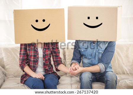 Couple with cardboard boxes on their heads with smiley face are sitting on floor after the moving house.