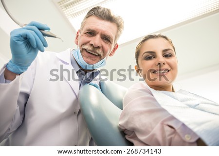 Senior dentist with his female client in dental clinic and looking at camera.