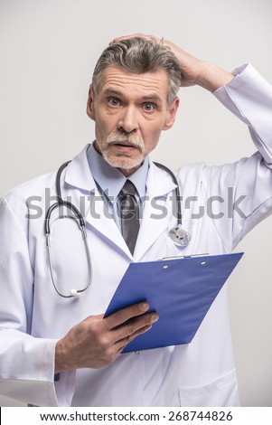 Senior male doctor standing with folder on grey background.