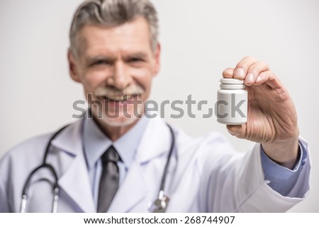 Senior male doctor holding pills on grey background. Focus on pills.