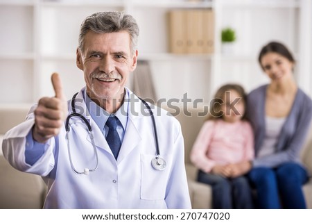 Senior male doctor is looking at the camera and smiling. Mother and her daughter on background.