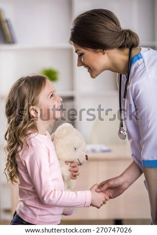 Side view  of young smiling female doctor and her little patient  with teddy bear.