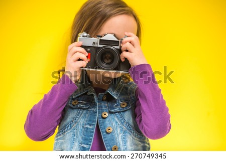 A little cute girl making photo on yellow background.