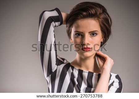 Portrait of young beauty woman in black-white shirt looking at camera on grey background.