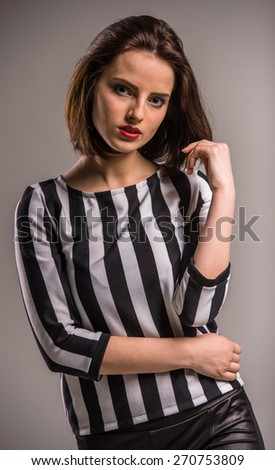 Young beauty woman in black-white shirt  looking at camera on grey background.
