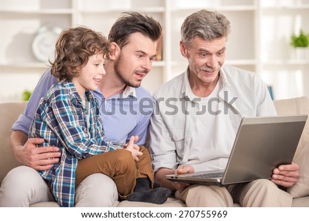 Generation portrait. Grandfather, father and son sitting and using laptop on sofa.
