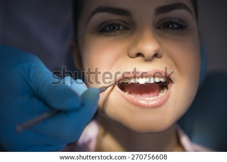 Dentist examining a patients teeth in the dentists chair under bright light at the dental clinic.