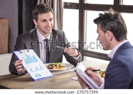 Smiling businessmen analyzing graphs during a business lunch.