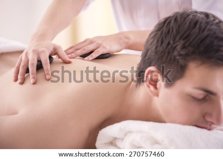 Female masseur doing back massage on man body with zen basalt stones in the spa salon.